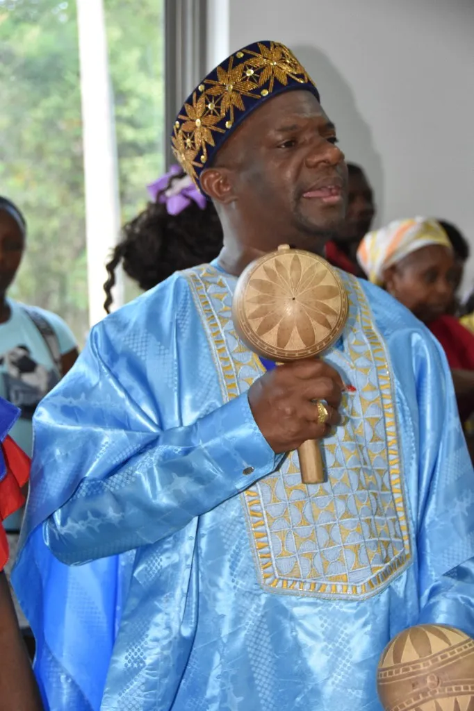 Pedro Adán Torres, con traje tradicional azul celeste bordado en dorado y kufi azul con flores doradas, canta con una maraca de totumo en la mano